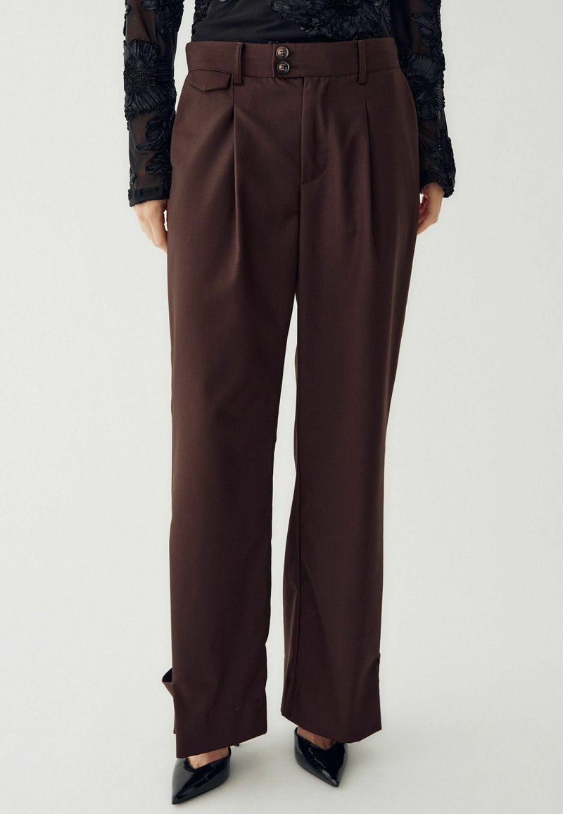 Smeđe, plisirane hlače s visokim strukom, opremljene s dvije dugmadi, prednjim džepovima i ravnim krojem. Glatka tekstura i krojena izrada.