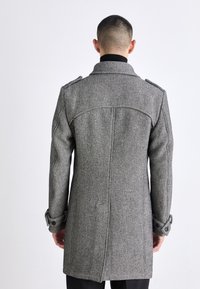 Houndstooth-rock i grått och svart, tillverkad av texturerat tyg. Har axelklaffar och knapplås på ärmsluten, skräddarsydd passform med en rak silhuett.