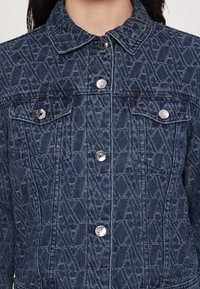 Jeansjacke mit einem strukturierten geometrischen Muster. Ausgestattet mit silbernen Druckknöpfen und Taschen. Dunkelblaue Farbe mit einem klassischen Kragen und durchgehender Knopfleiste.