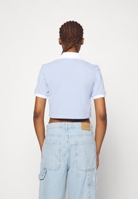 Polo shirt corto di colore azzurro chiaro con maniche corte, colletto bianco, abbinato a pantaloni cargo in denim chiaro a vita alta con tasche a toppa.