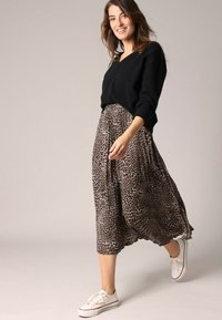 Pull noir à col en V, jupe midi à imprimé animal en beige et marron, et baskets blanches avec des accents rouges. La jupe a un design fluide.