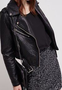 Veste de motard en cuir noir avec des fermetures éclair argentées, une finition texturée et une coupe ajustée, associée à un haut noir et une jupe à sequins.