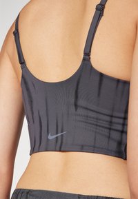 Sutiã desportivo cinza com alças ajustáveis, apresentando uma textura riscada subtil e um pequeno logótipo da Nike cinza na parte inferior.