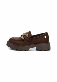Mocasín de ante marrón con una gruesa suela de goma texturizada. Presenta un hebilla decorativa en tono dorado y un sencillo cosido a lo largo de la parte superior.