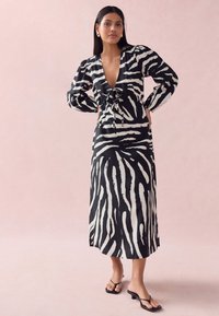 Black and white zebra-striped long dress with a deep V-neck, drawstring waist, and puffed sleeves. Smooth fabric, knee-length, paired with black sandals.