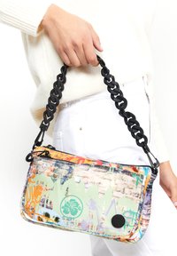 Färgglad handväska med graffiti-mönster i rektangulär form, tillverkad av texturerat material. Har en tjock svart kedjesnodd och dragkedjestängning.