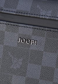Grijze portemonnee met patroon, gemaakt van getextureerd materiaal, met een subtiel geruit ontwerp en een metalen "JOOP!"-logo. Ritsdetails zijn zichtbaar.