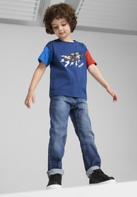 Blå og rød T-shirt med korte ærmer, der har et grafikdesign med lyn og en bil, parret med opsmallede denimjeans og sorte sneakers.