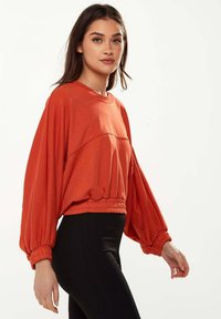 Red cropped sweatshirt with oversized, balloon sleeves and a ribbed hem. Paired with black ribbed leggings for a contrasting look.