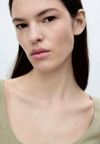 Primo piano del viso di una persona con pelle liscia, capelli scuri e labbra neutre. Lo sfondo è chiaro, il che aumenta il focus sulle caratteristiche facciali.