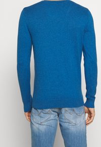 Pull tricoté bleu à manches longues et col rond. Présente une texture lisse et un détail de ourlet côtelé. Associé à un jean bleu clair.