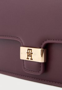 Borsa a mano in pelle viola con chiusura in metallo dorato con logo. Texture liscia con cuciture pulite e un design strutturato.