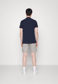 Granatowa koszulka polo, beżowe szorty, białe tenisówki. Casualowy design, krótkie rękawy i lekko dopasowany krój. Gładka faktura, minimalne detale.