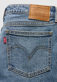 Πίσω τσέπη ανοιχτόχρωμου τζιν Levi's με πορτοκαλί ραφές, κόκκινη ετικέτα Levi's και καφετί δερμάτινο ταμπελάκι της μάρκας στη μέση.