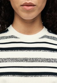 Pull à côtes blanc et marine à rayures avec un col rond, présentant des rayures de différentes épaisseurs et un motif en tricot texturé.