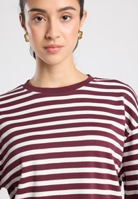 Langärmliges Hemd mit burgunderroten und weißen Streifen, Rundhalsausschnitt. Weicher Baumwollstoff, lockere Passform, dezente Rippenstruktur am Halsausschnitt.