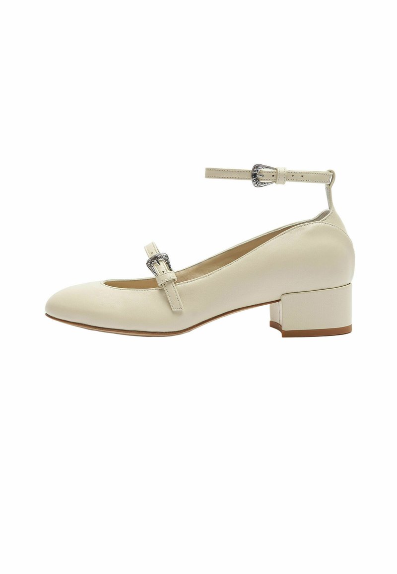 Zapato de cuero blanco con tacón cuadrado, punta redondeada, correa en el tobillo y hebilla decorativa. Textura suave y diseño sencillo.