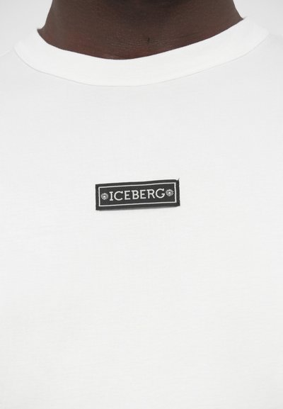 Λευκό κοντομάνικο βαμβακερό μπλουζάκι, με ορθογώνια μαύρη ετικέτα που φέρει λευκή επιγραφή "ICEBERG" και διακοσμητικές λεπτομέρειες.