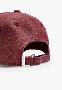 Gorra burdeos hecha de tela texturizada con un visera curvada, correa ajustable con un anillo metálico y una pequeña etiqueta etiquetada como "SCALPERS."