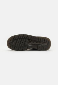 Suela de zapato de goma negra con diseño de textura, que presenta surcos profundos para tracción y una forma plana, diseñada para durabilidad y comodidad.