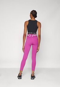 Top nero senza maniche e leggings rosa con una vita alta. I leggings hanno la scritta "NIKE PRO" in bianco stampata. Scarpe da ginnastica nere.