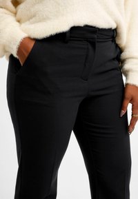 Svarta skräddarsydda byxor med en slät yta, med sidofickor och slim fit. Kombineras med en fluffig krämfärgad tröja.