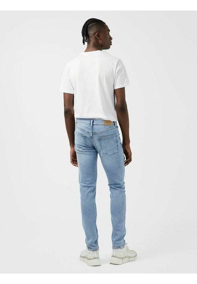 Lichtblauwe denim jeans met een slim fit, achterzakken, leren patch op de taille, gecombineerd met een eenvoudig wit T-shirt en witte sneakers.