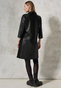 Schwarzer Leder-Mantel mit lässiger Passform, Dreiviertelärmeln und knielangem Design. Glatte Textur mit Kragen und geradem Saum.