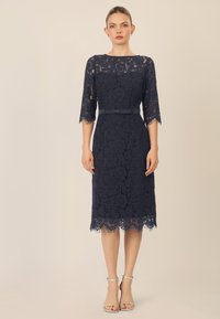 Navy lace-mekko, jossa on kolmanneksen mittaiset hihat, aallotettu helma ja irrotettava satiinivyö. Yhdistetty hopeisiin nilkkaketjullisiin korkokenkiin.