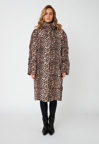Geacă puffer cu imprimeu leopard, guler înalt, mâneci lungi și textură matlasată. Pantaloni ajustați negri și cizme negre până la gleznă completează ținuta.