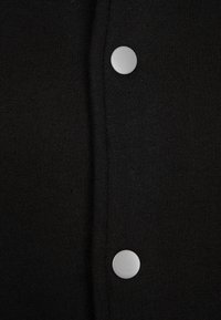 Gros plan sur un tissu noir avec deux boutons-pression ronds en argent fermés le long de la couture verticale.