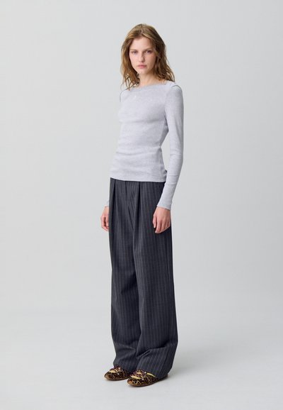 Maglietta grigia chiara a maniche lunghe con vestibilità slim, abbinata a pantaloni larghi a righe sottili scuri a vita alta e ballerine con stampa animale.