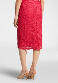 Gonna a matita rossa in pizzo con motivo floreale, lunghezza al ginocchio, con orlo ondulato e chiusura con cerniera sul retro. Indossata con sandali con tacco trasparente.