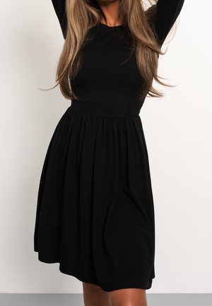 Abito nero realizzato in tessuto liscio, caratterizzato da maniche lunghe, corpino aderente e gonna svasata che si raccoglie in vita.