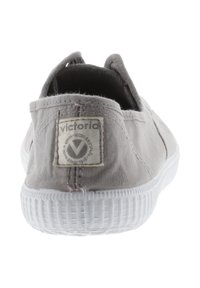Zapatilla de lona gris claro vista desde atrás, con suela blanca y una etiqueta de tela cosida con la marca "victoria".