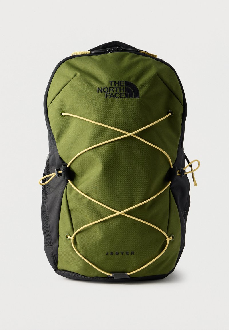 Πράσινο και μαύρο σακίδιο North Face Jester με κίτρινο ελαστικό κορδόνι σε σχήμα σταυρού μπροστά και πλέγμα πλαϊνές τσέπες σε λευκό φόντο.