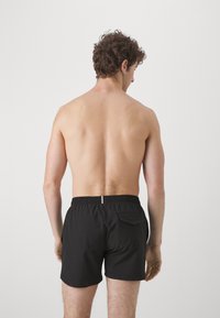 Sorte svømmebukser med elastisk talje, der har en lille baglomme. Stoffet ser glat og let ud.