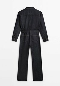 Czarna dżinsowa kombinezon z długim rękawem, z guzikami na mankietach, tylnej kieszeniami, pętlami na pasek i prostymi nogawkami, pokazany z tyłu na białym tle.