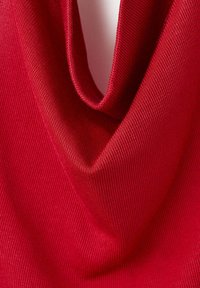 Tissu tricoté rouge drapé pour former un col bénitier doux montrant une fine texture côtelée et une couleur vibrante.