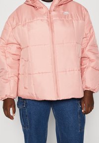 Rosa puffjacka med dragkedja fram, elastiska ärmslut och huva. Har en puffy quiltad design och en liten vit logga på bröstet.