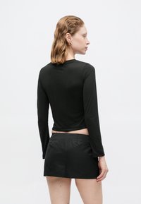 Must ühepikkade varrukatega must topp, millel on ühtlane disain ja pehme tekstuur, koos musta mini seelikuga. Riietus omab lihtsat ja modernset välimust.