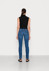 Blå denim skinny jeans med två bakfickor som har sydda detaljer, tillsammans med en ribbad svart ärmlös topp.