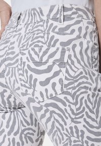 Weiße Hose mit einem dunkelgrauen abstrakten Muster, das Zebrastriche ähnelt, mit mehreren Taschen und einer taillierten Passform.