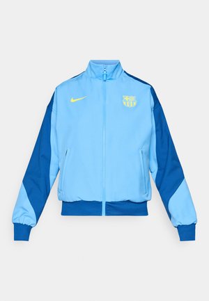 Chaqueta azul claro con cremallera, mangas azul oscuro, puños elásticos y dobladillo acanalado. Cuenta con un logo amarillo de Nike y un emblema del FC Barcelona.