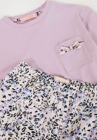 Top de manga corta lila con detalle de bolsillo, combinado con pantalones cortos de estampado en blanco, lavanda y leopardo negro.