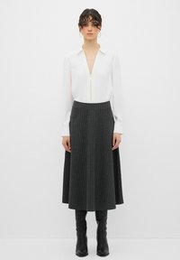 Blusa bianca con zip e colletto, abbinata a una gonna midi nera a righe e stivali neri al ginocchio, creando un outfit formale.
