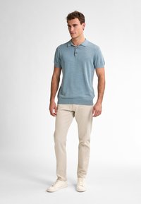 Světle modrá polokošile s krátkým rukávem, límečkem a třemi knoflíky, v kombinaci s béžovými slim-fit kalhotami a bílými teniskami.