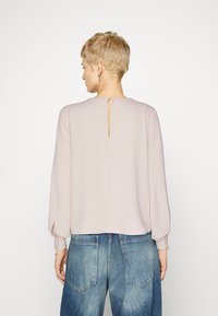 Light pink top with long sleeves, round neckline, and back keyhole detail. Paired with blue denim jeans featuring a logo patch.