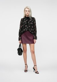 Blusa nera a fiori con scollatura a fiocco, abbinata a una mini gonna in pelle bordeaux. Gli accessori includono una piccola borsa nera e sandali neri con cinturini.