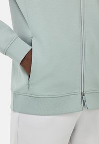 Felpa zip a pullover verde chiaro con polsini e bordo a costine, tasca laterale con zip e materiale in felpa morbido per una vestibilità comoda.